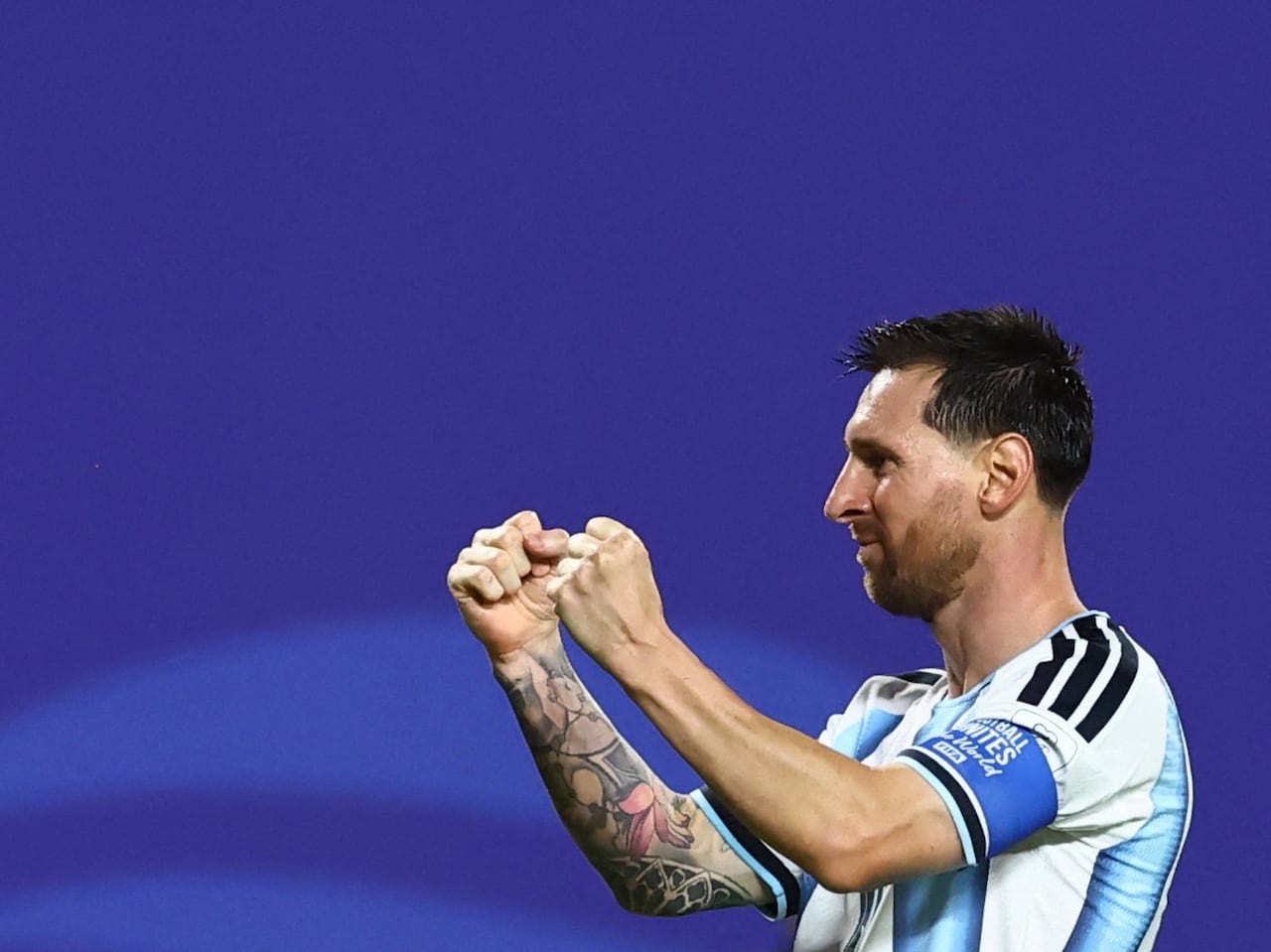 Image 4: A male soccer player raising both fists in triumph and smiling, against a blue background on the pitch.