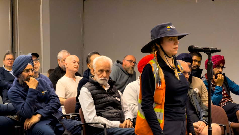 Image 13: A woman standing at a mic people sitting in chairs in the background.