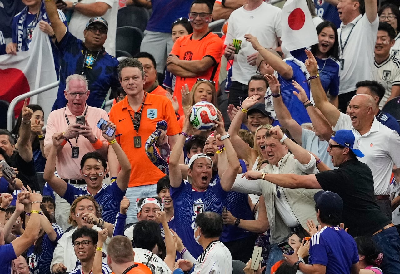 Image 6: A man surrounded by fans holds up a soccer ball.