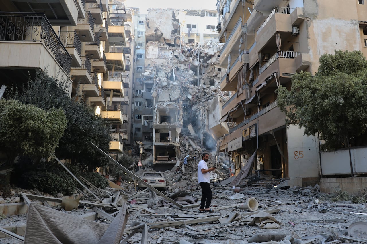 Image 5: A man is shown from a distance standing on a street filled with concrete and other debris as multistorey buildings are shown damaged all around him.